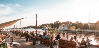 Menschen sitzen bei Sonnenschein unter freiem Himmel am Kieler Sandhafen