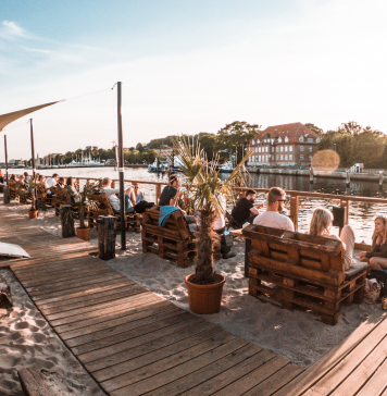 Menschen sitzen bei Sonnenschein unter freiem Himmel am Kieler Sandhafen