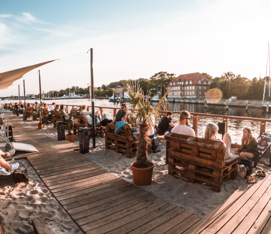 6 angesagte Kieler Beach Bars Menschen sitzen bei Sonnenschein unter freiem Himmel am Kieler Sandhafen