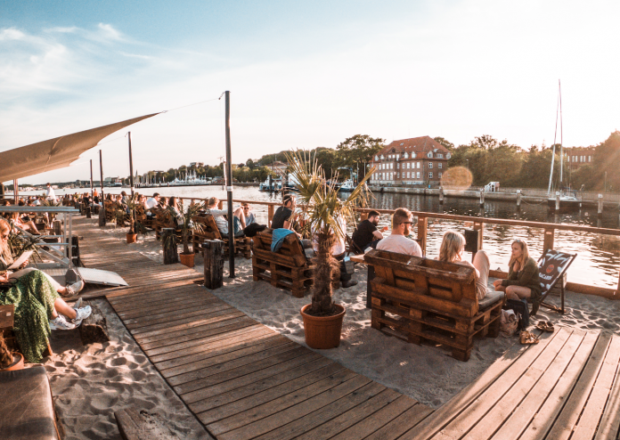 Menschen sitzen bei Sonnenschein unter freiem Himmel am Kieler Sandhafen